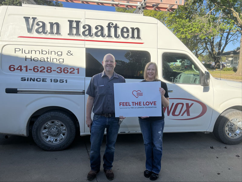 A man and a woman standing in front of the Van Haaften truck holding a Feel the Love sign